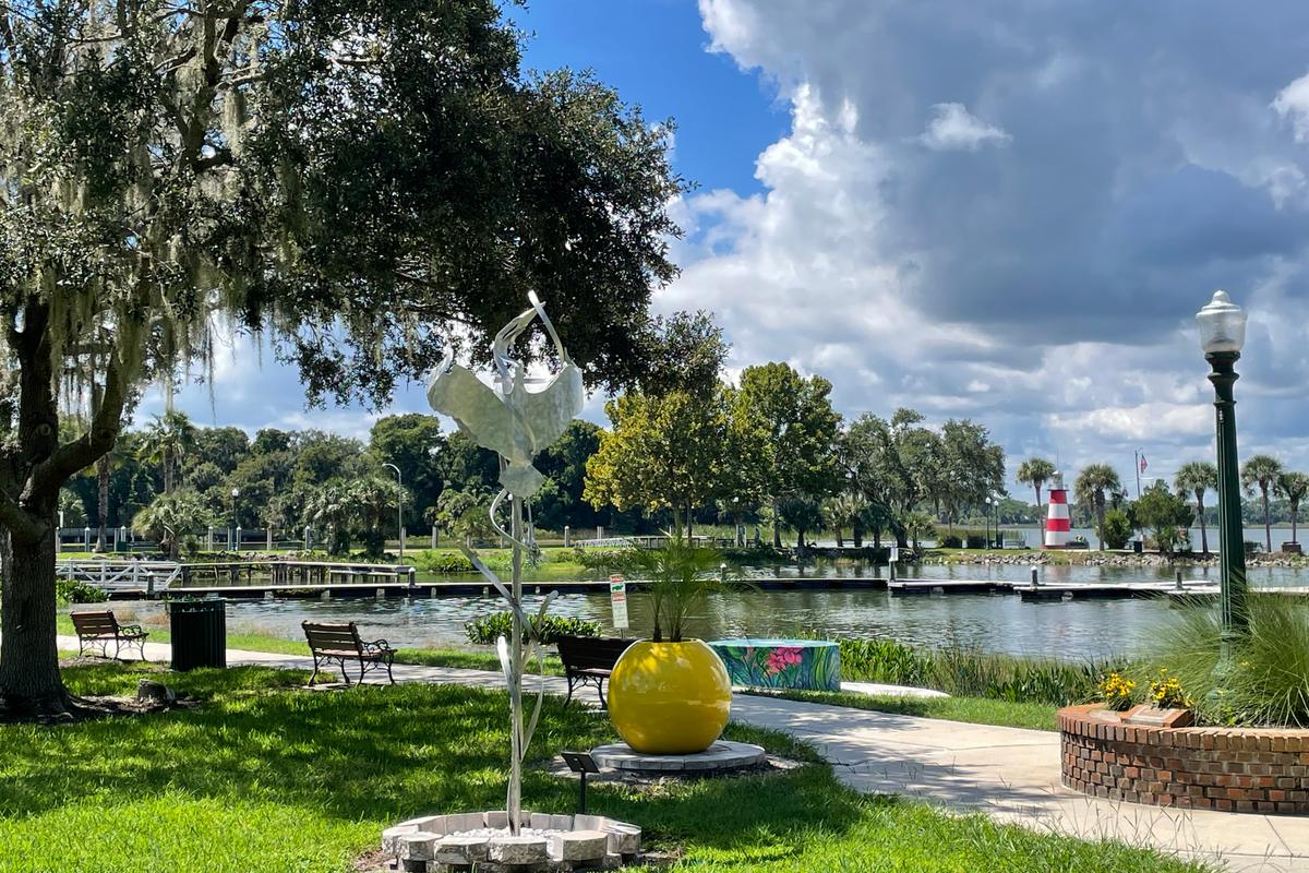Grantham Point Park on Lake Dora with a sculpture, a yellow planter, and the Mount Dora lighthouse in the distance, the hometown setting for these Mount Dora home seller resources