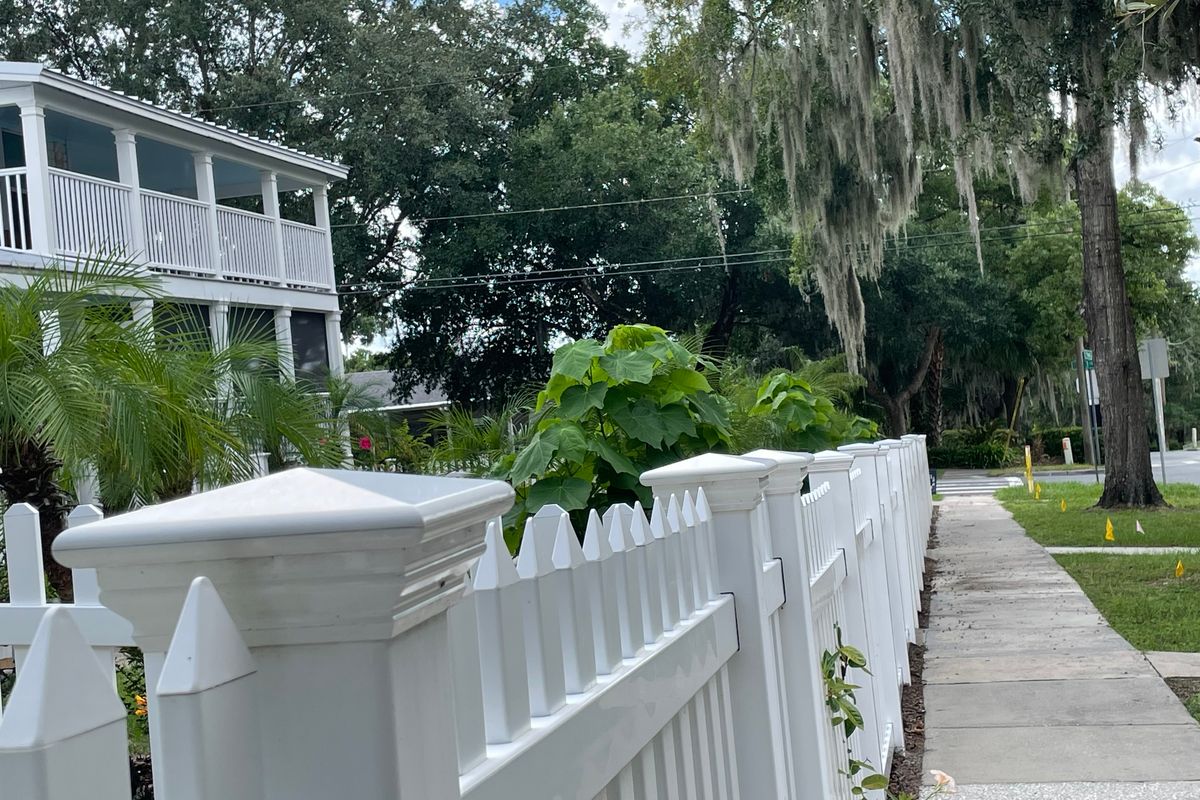 A historic neighborhood in Mount Dora White picket fence and sidewalk under moss-draped oaks beside a two-story porch home in one of the historic neighborhoods in Mount Dora