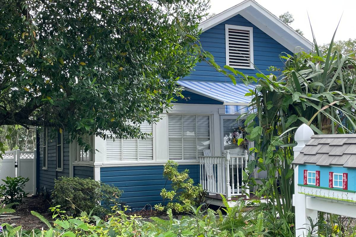 Blue cottage and garden in Mount Dora Blue clapboard cottage with white trim and a striped awning, with a painted miniature house on a post in the garden, in Mount Dora