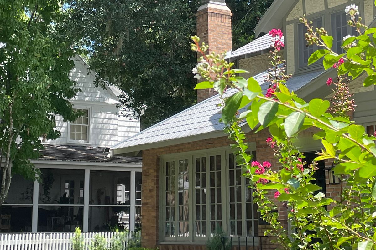 Brick bungalow with tall multi-pane windows beside a white older home, framed by crepe myrtle blooms in Mount Dora