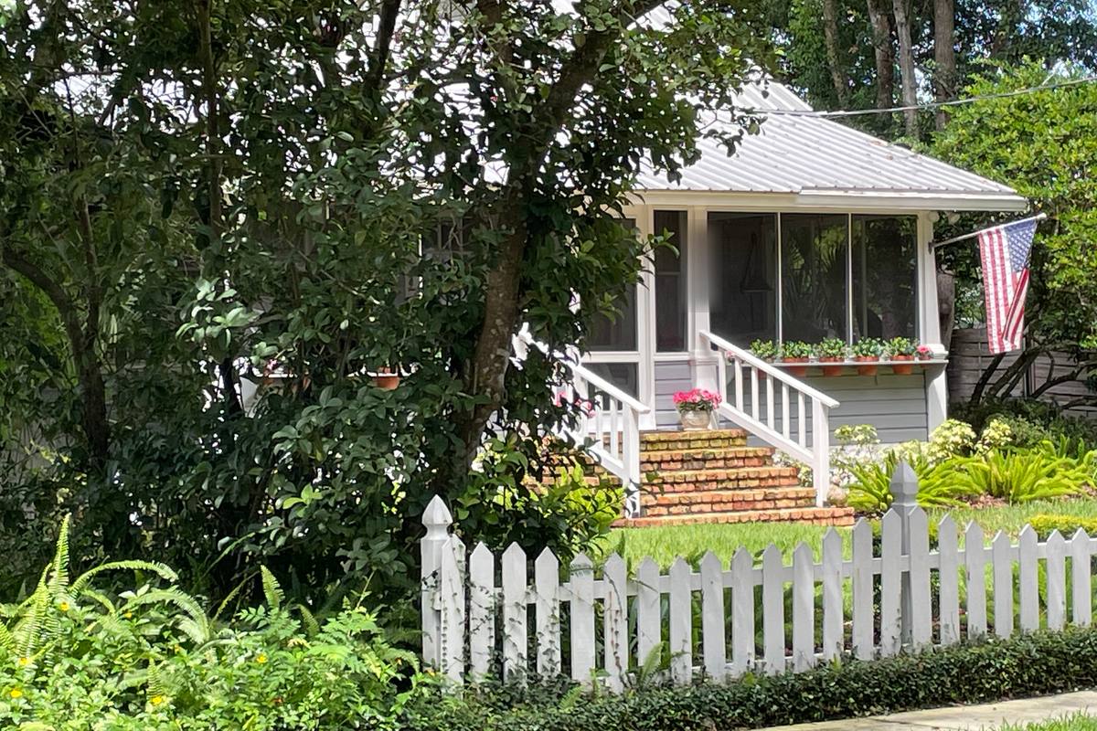 Brick steps leading up to the screened front porch of a small white cottage behind a picket fence in Mount Dora