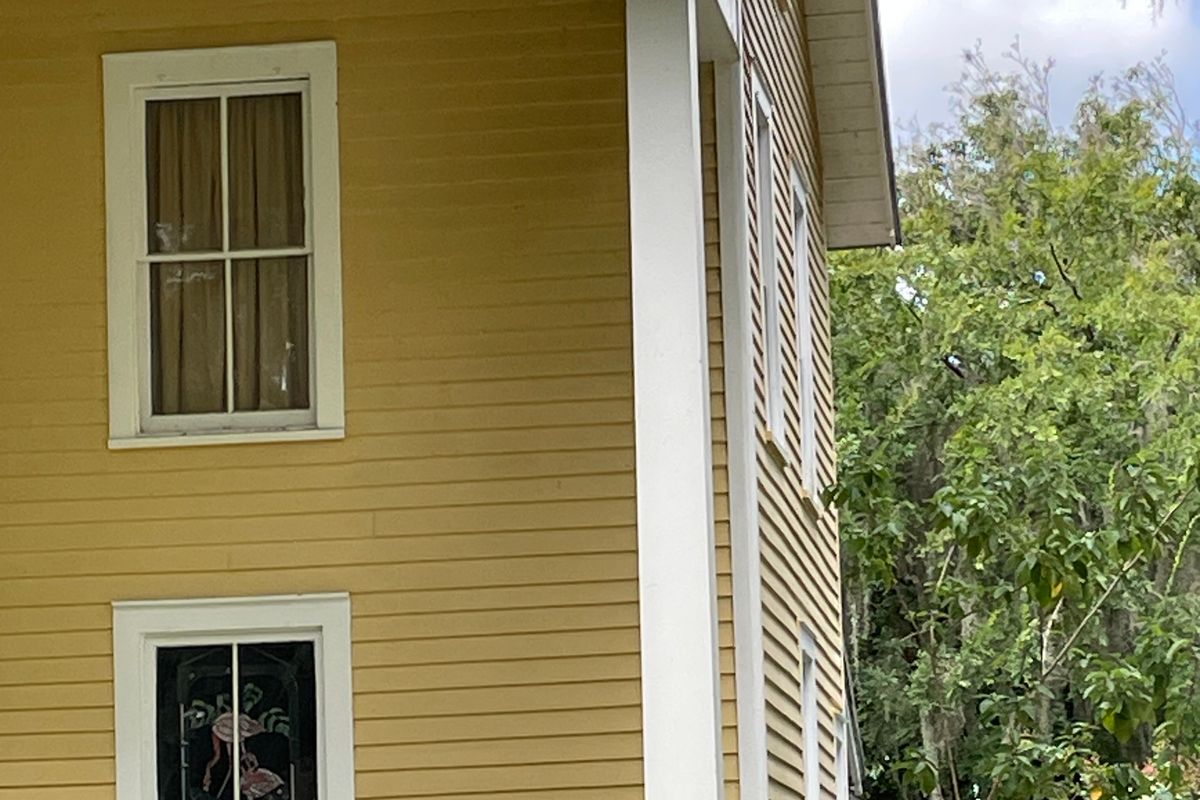 Double-hung windows with wide white trim on the yellow clapboard wall of an older two-story home in Mount Dora